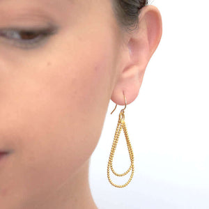 Close up front view of woman wearing pair of gold beaded wire teardrop shaped earrings on earwire.