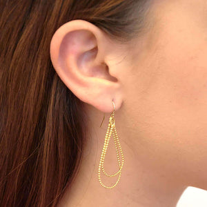 Close up side view of woman wearing pair of gold beaded wire teardrop shaped earrings on earwire.