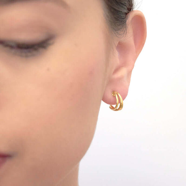 Close up front view of woman wearing pair of small curved gold ear cuff earrings.