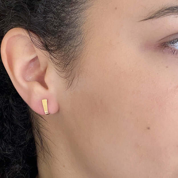 Close up front view of woman wearing pair of tiny gold post cuff earrings that wrap around earlobe.