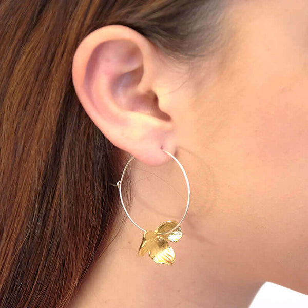 Close up side view of woman wearing pair of earrings of gold orchid petals on a silver hoop.
