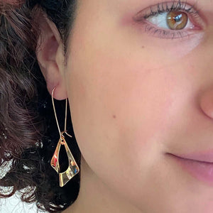 Close up front view of woman wearing pair of gold earrings, flat diamond shape with oval cutout on french earwire.