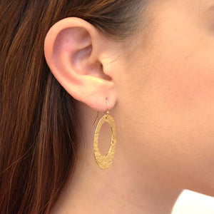 Close up side view of woman wearing pair of gold hammered oval earrings on earwire.