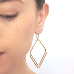 Close-up front view of woman wearing a pair of gold rhombus shaped earrings.