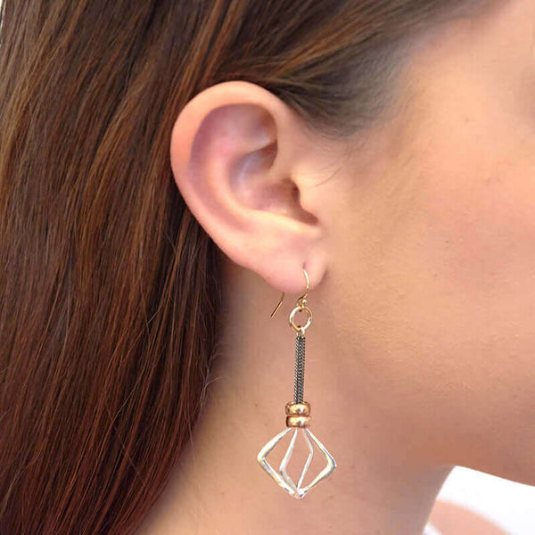 Close-up side view of woman wearing dark chain dangle earrings with cast silver rhombus.