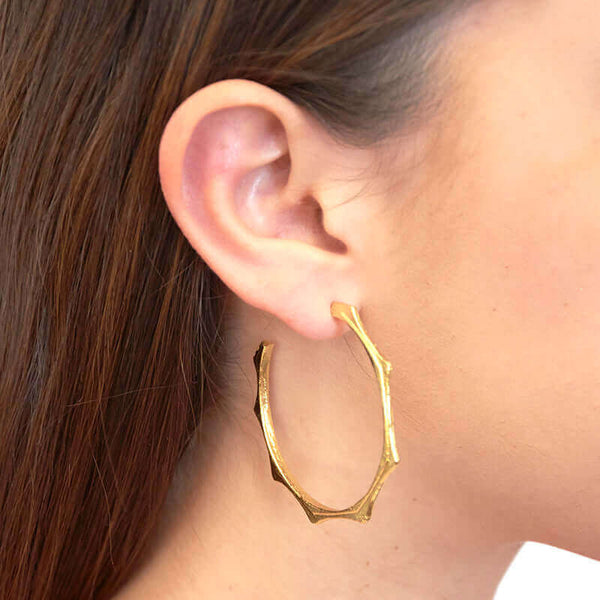 Close-up side view of woman wearing a pair of gold cast hoop earring on post with sun motif.