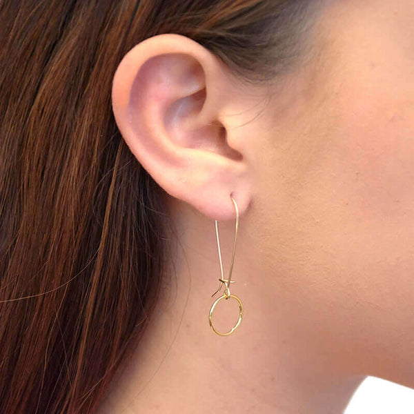 Close-up side view of woman wearing a pair of gold circle earrings on long french earwire.