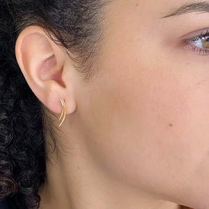 Close-up side view of woman wearing a pair of gold earrings of 2 curved swoops on posts, hanging down.