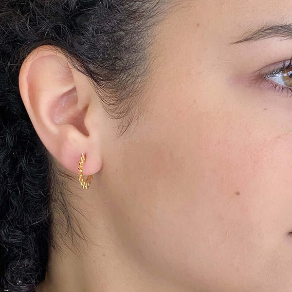 Close-up side view of woman wearing a pair of cast curved spiky gold earrings on posts.