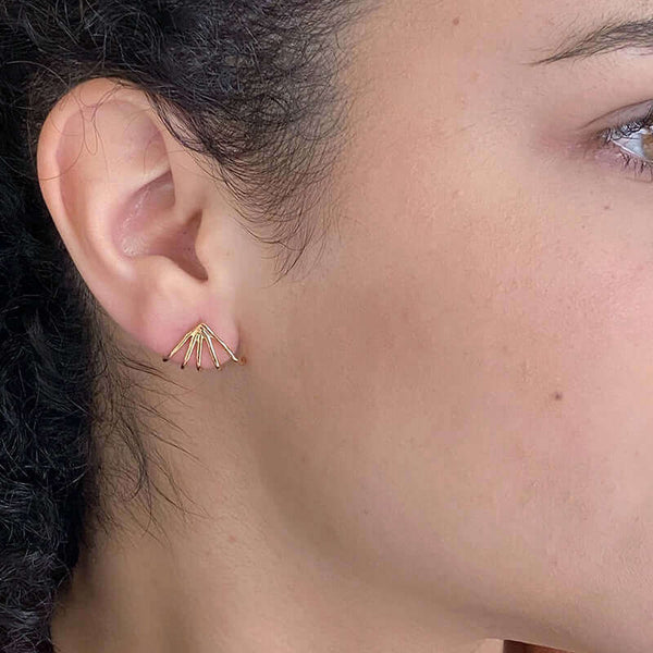 Close-up side view of woman wearing a pair of gold earrings with 5 gold wires that wrap around earlobes.