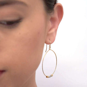 Close-up front view of woman wearing a pair of silver hoop earrings with small gold and silver square beads on hoop.