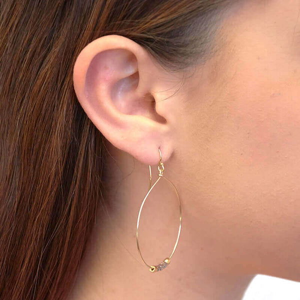 Close-up side view of woman wearing a pair of silver hoop earrings with small gold and silver square beads on hoop.