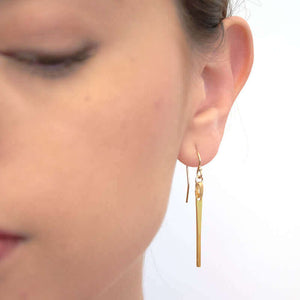 Close-up front view of woman wearing a pair of gold drop earrings, of a flattened bar on earwire.