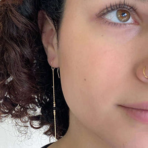 Close-up front view of woman wearing a pair of gold earrings, gold chain with black bead details.