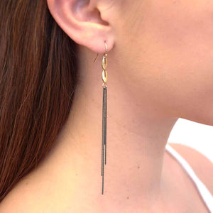 Close-up side view of woman wearing a pair of dark chain earrings, multiple dark chains hanging on gold links.