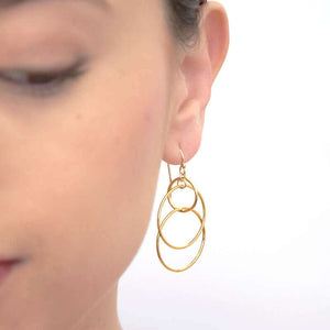 Close-up front view of woman wearing a pair of gold earrings, 3 interlocked circles on earwire.