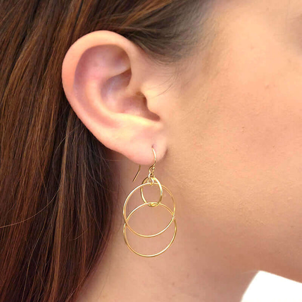 Close-up side view of woman wearing a pair of gold earrings, 3 interlocked circles on earwire.