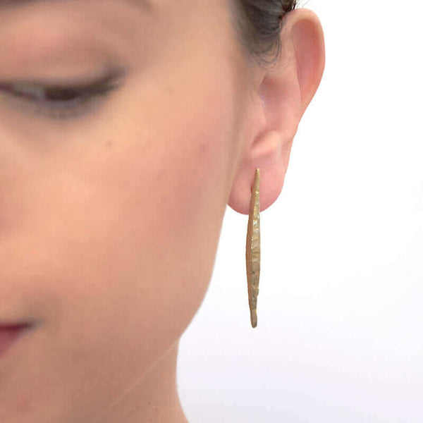 Close-up front view of woman wearing a pair of brass spike earrings on posts.