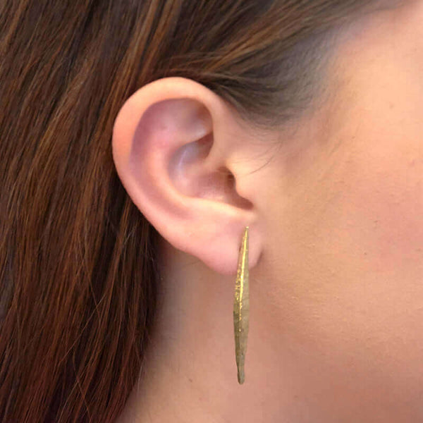 Close-up side view of woman wearing a pair of brass spike earrings on posts.