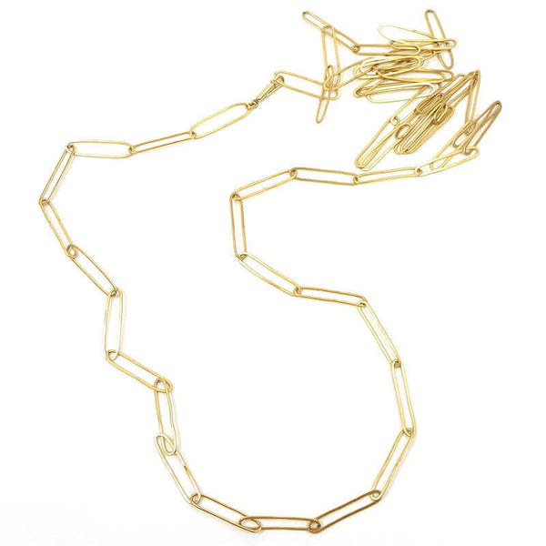 Gold longated link necklace with clean modern design laid naturally on surface.
