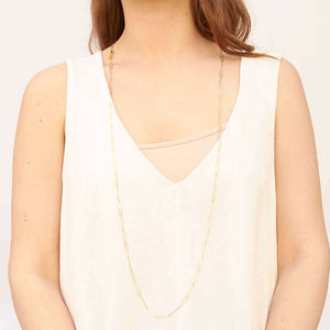 Woman wearing a long gold elongated link necklace, that hangs down to mid torso.