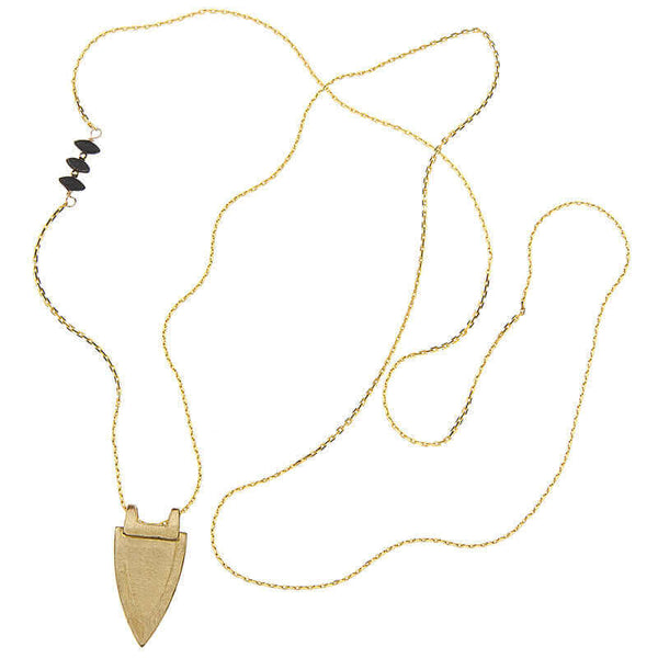 Long gold necklace with shield shaped pendant and black bead accents, chain laid out to show length of necklace.