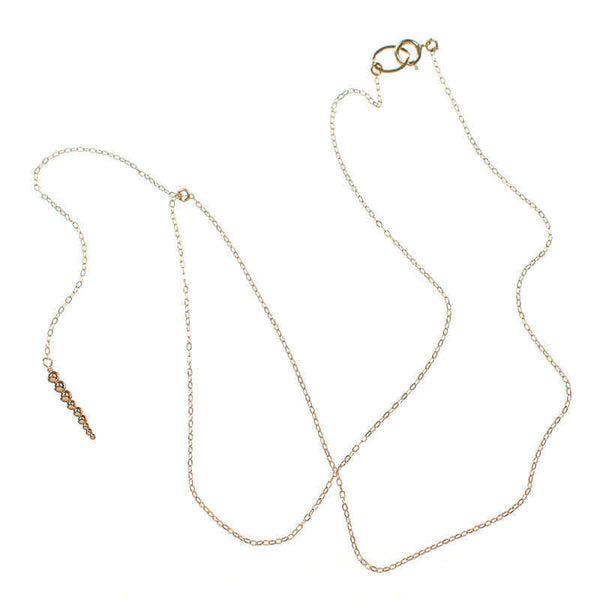 Delicate gold chain necklace with drop pendant of small gold beads, laid out showing clasp.