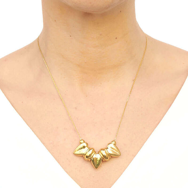 Woman wearing gold necklace, thin gold chain with pendant of three large heart-shaped beads.