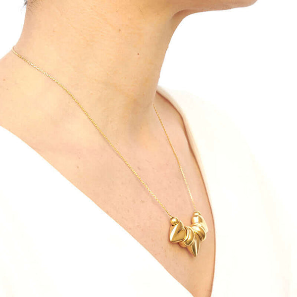 Woman wearing gold necklace, thin gold chain with pendant of three large heart-shaped beads, shown from side angle.