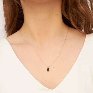Woman wearing delicate gold chain necklace with small black beads as pendant.