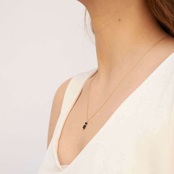 Woman wearing delicate gold chain necklace with small black beads as pendant, shown form side angle.