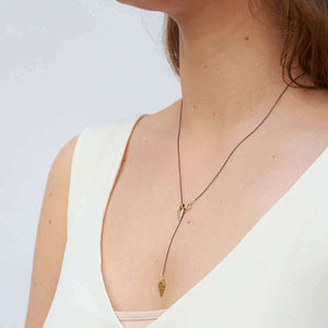 Woman wearing black chain necklace with both brass arrowheads in front, shown form side angle.