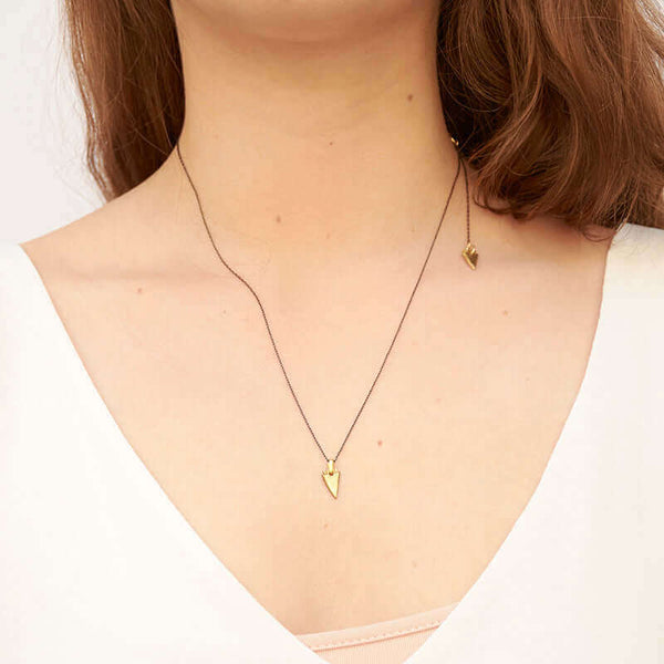 Woman wearing black chain necklace with one brass arrowhead in front, and one at neck.