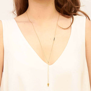 Woman wearing gold necklace, long arrow pendant, chain with black bead accents.