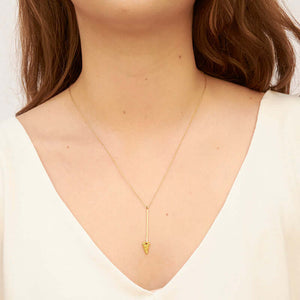 Woman wearing gold necklace, short arrow pendant, chain with black bead accents.