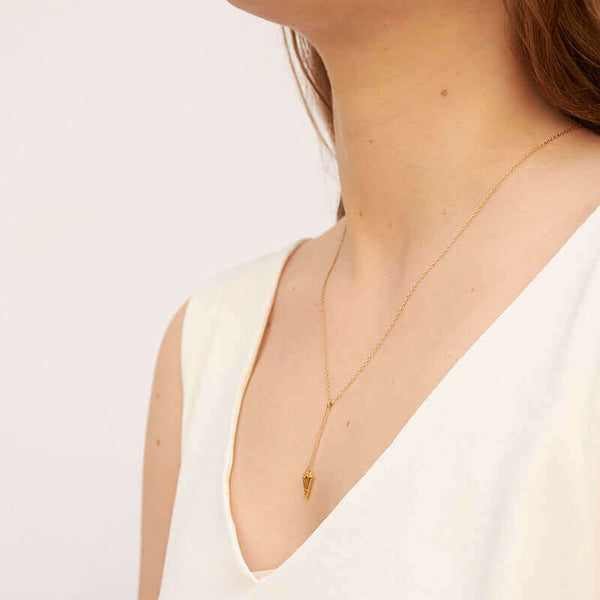 Woman wearing gold necklace, short arrow pendant, chain with black bead accents, shown from side angle.