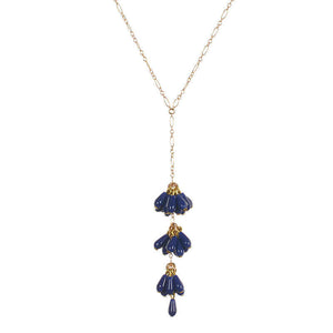 Close-up of delicate gold chain necklace with drop pendant of 3 bunches of dark blue beads with single bead at end.
