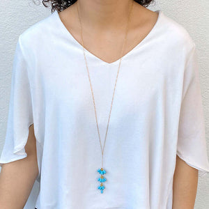 Woman wearing gold chain necklace with pendant of 3 bunches turquoise beads with single bead at end.