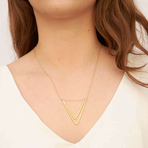 Woman wearing delicate gold chain necklace with two nested v-shaped pendants.
