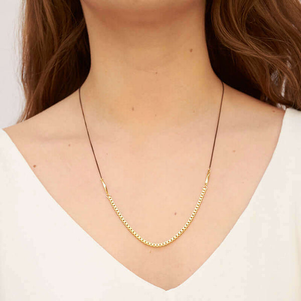 Woman wearing necklace with black upper chain and gold box chain on the bottom.