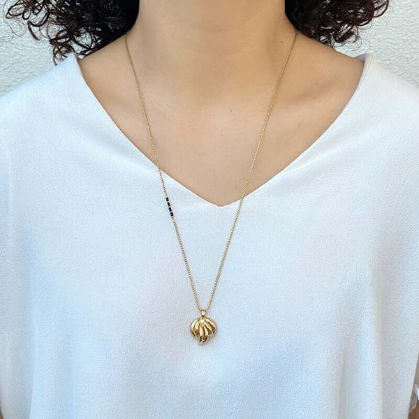 Woman wearing gold chain with black bead accent on side, with pendant of bunch of curved pieces.