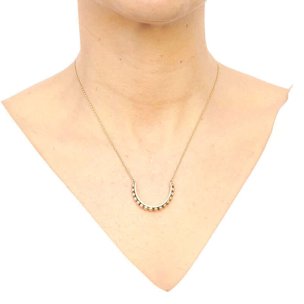 Woman wearing gold chain with half-circle beaded bar as pendant, worn short.