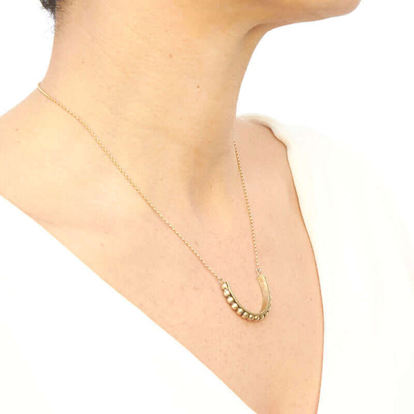 Woman wearing gold chain with half-circle beaded bar as pendant, shown form side angle.