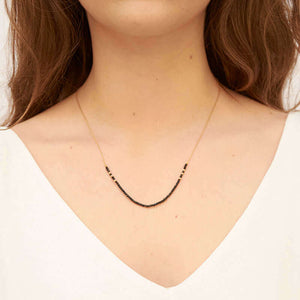 Woman wearing gold necklace with small black beads on the bottom section.
