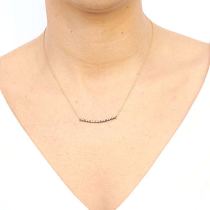 Woman wearing gold chain necklace with curved beaded bar pendant.