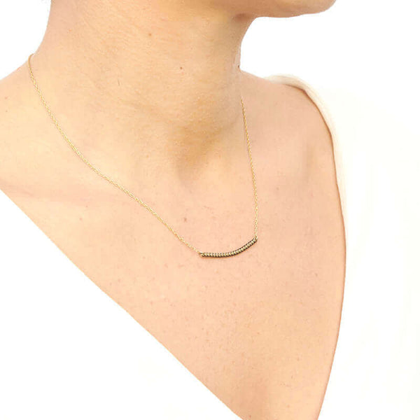 Woman wearing gold chain necklace with curved beaded bar pendant, shown from side angle.
