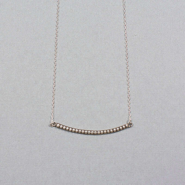 Close-up of silver chain necklace with curved beaded bar pendant.