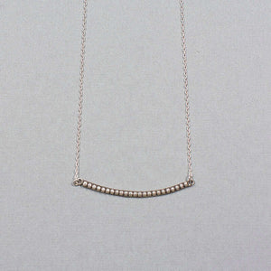 Close-up of silver chain necklace with curved beaded bar pendant.