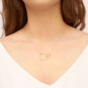 Woman wearing gold chain necklace with small and large interlocking circles as pendant.