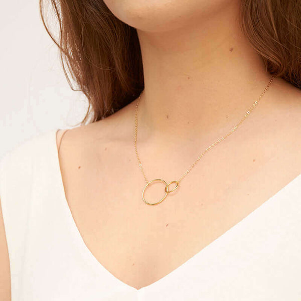 Woman wearing gold chain necklace with small and large interlocking circles as pendant, shown from side angle.
